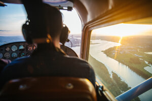 View of a pilot in a cockpit while flying over a river at sunrise