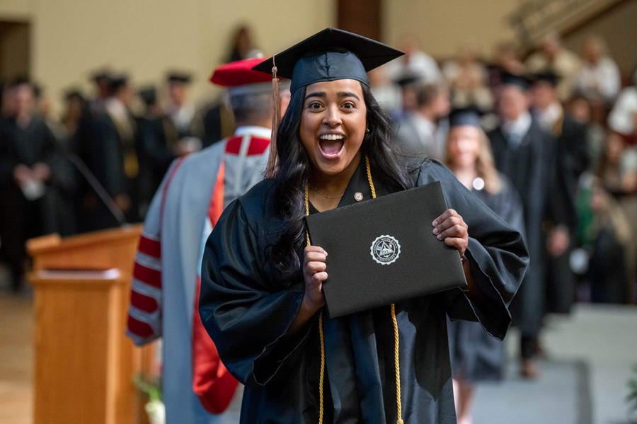 A smiling graduate in a cap and gown holds up her diploma 