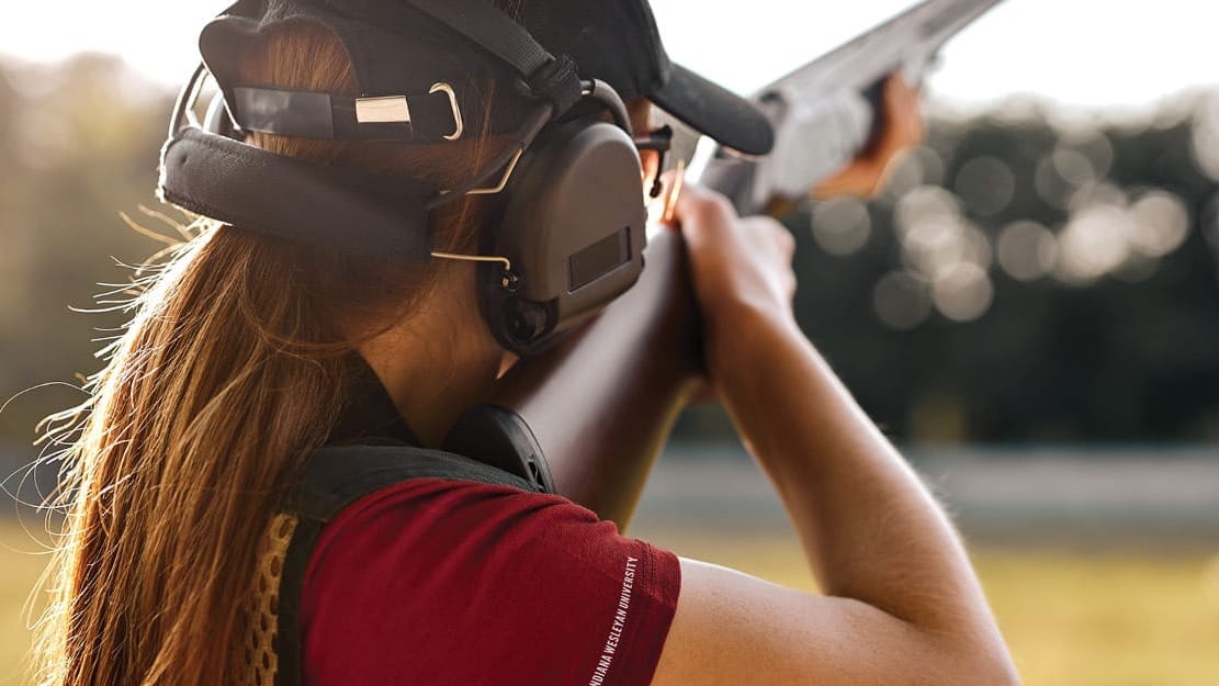 Back view of girl with ear protection shooting a shotgun