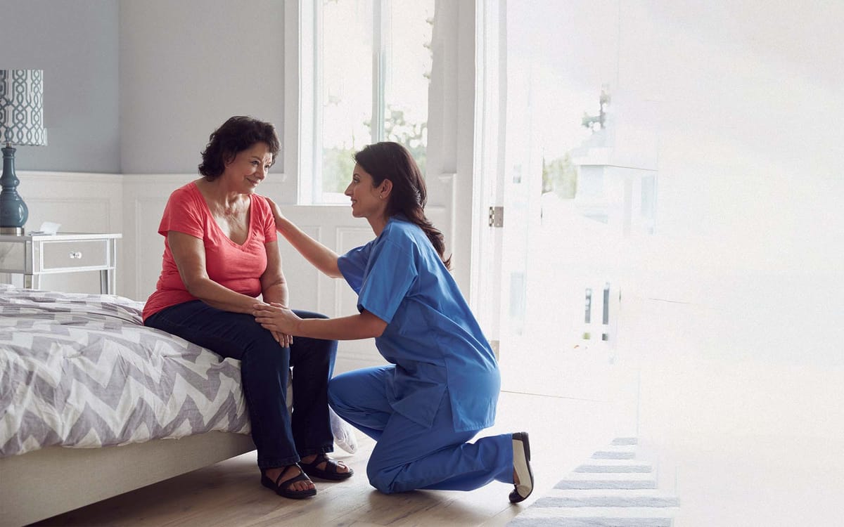 Nurse kneeling next to a woman sitting on a bed