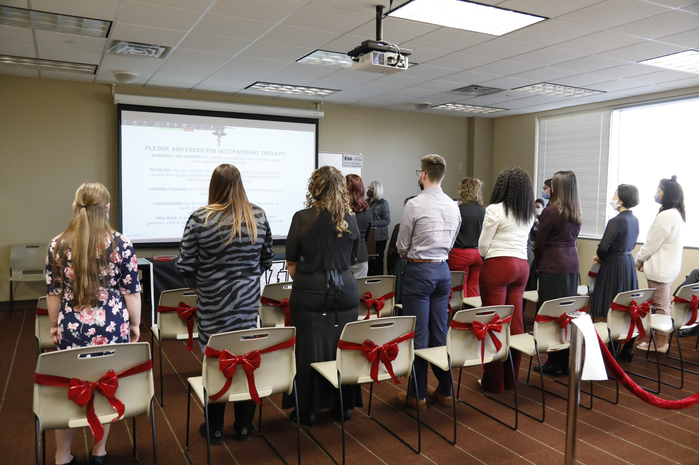 A group of students stand for the pledge and creed for occupational therapy.