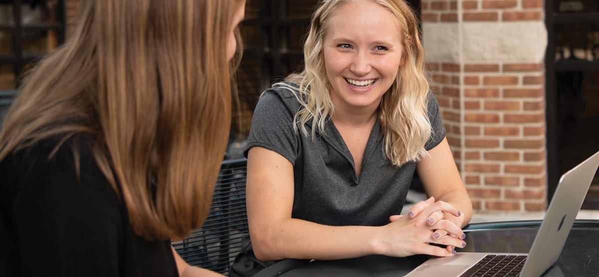 Female student smiling with another female student in front of a computer