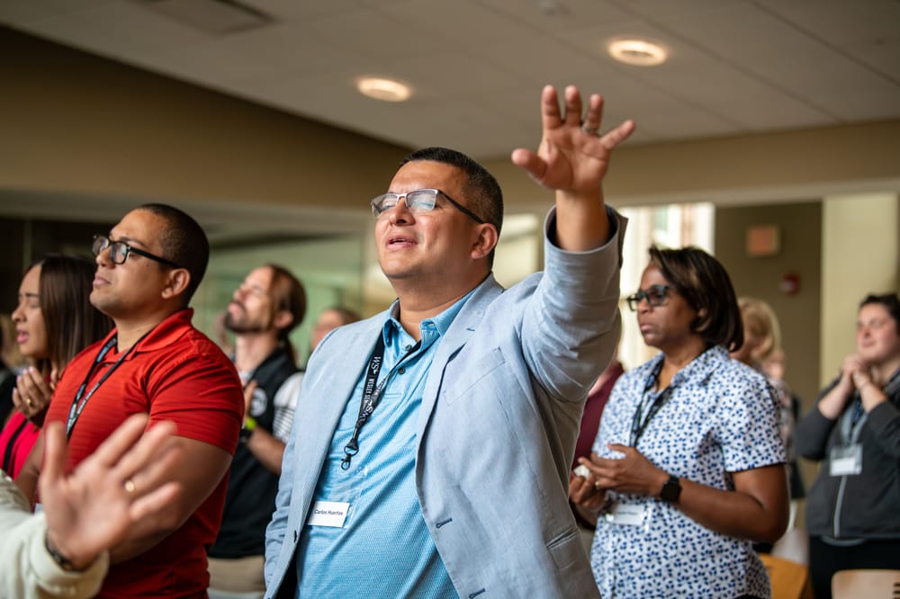 Man with hand raised in worship among a group of people.