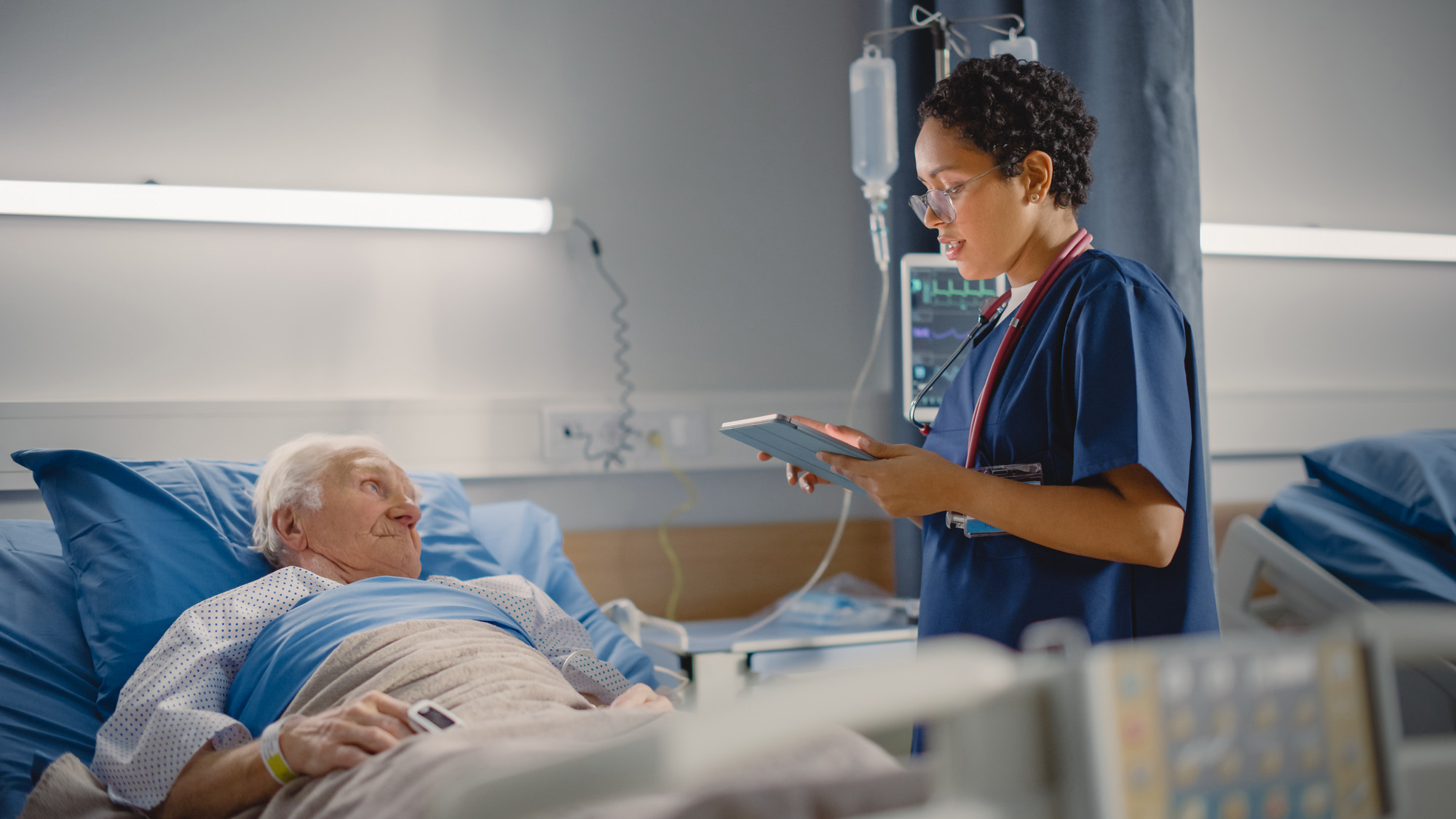 Nurse talking to an elderly man in hospital bed