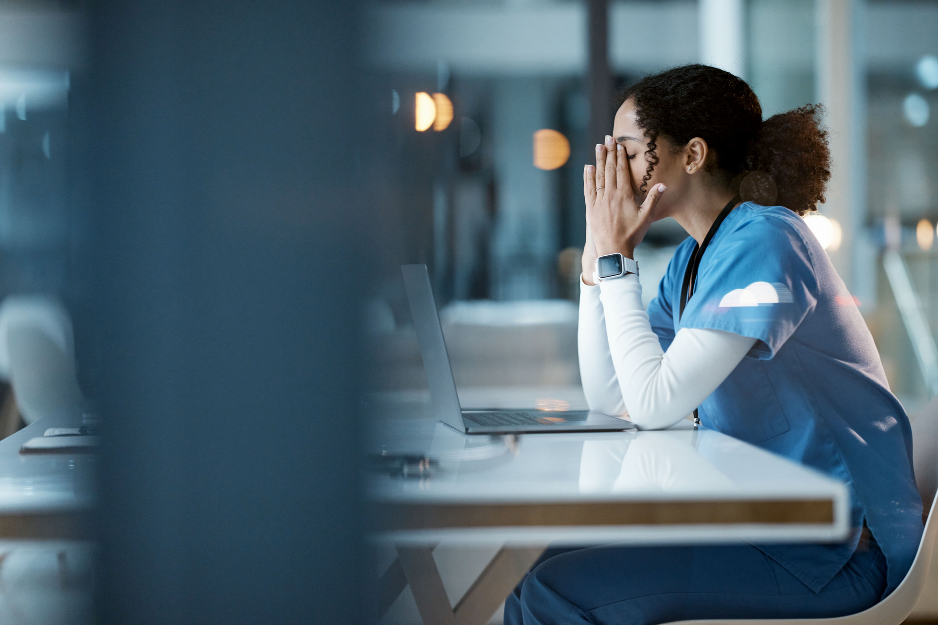 Nurse sitting at table in front of laptop with hands covering her eyes