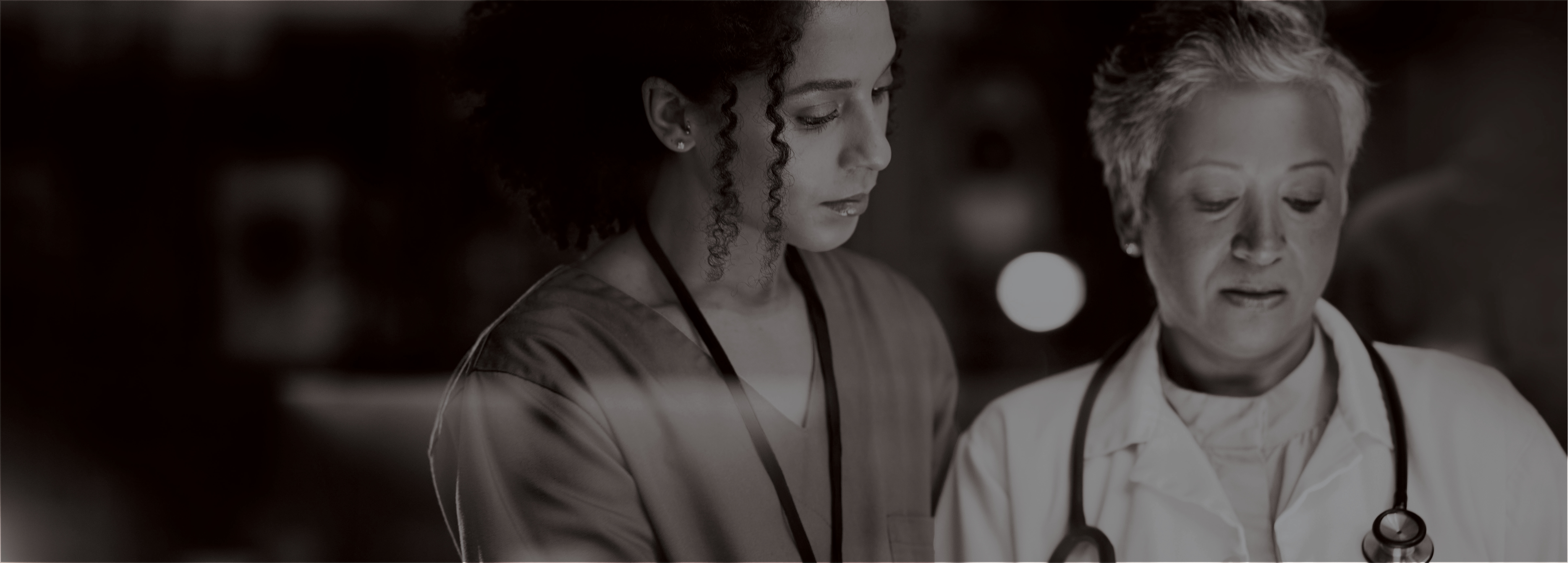 Grayscale image of nurse and doctor looking down, mostly likely at a file not shown in the photo.