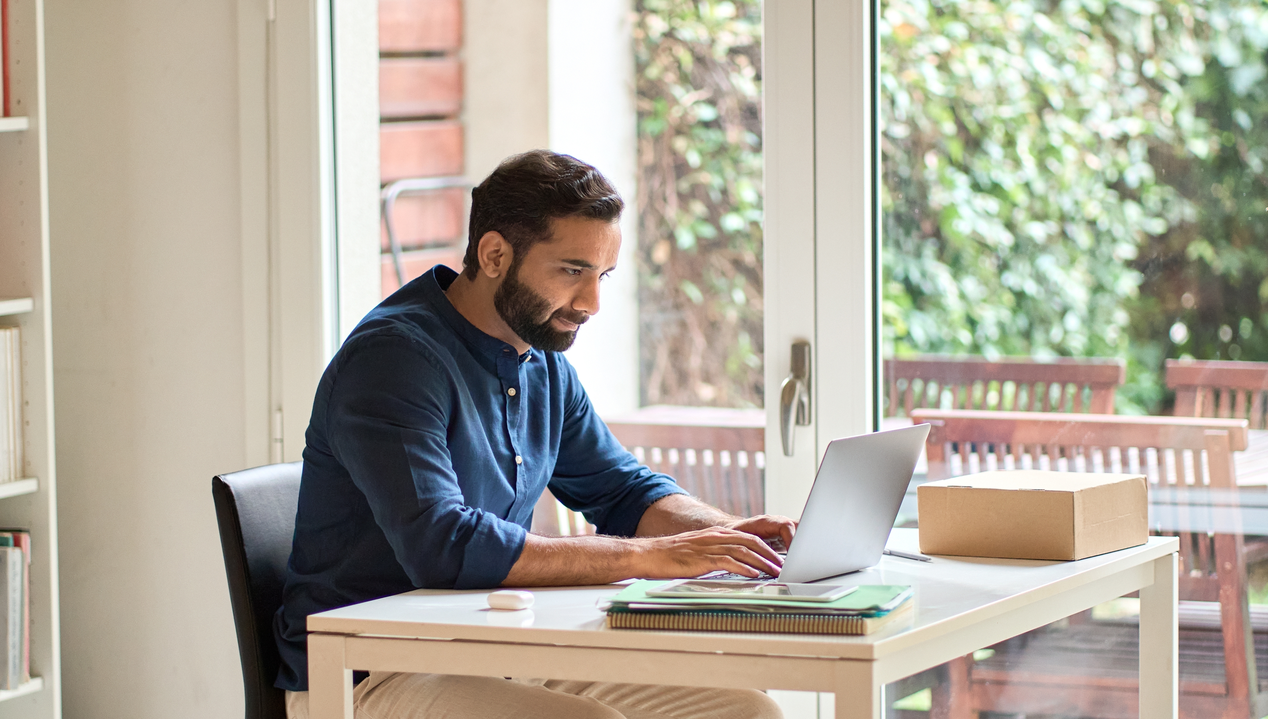 Indian man using laptop for remote learning while sitting at home office table.