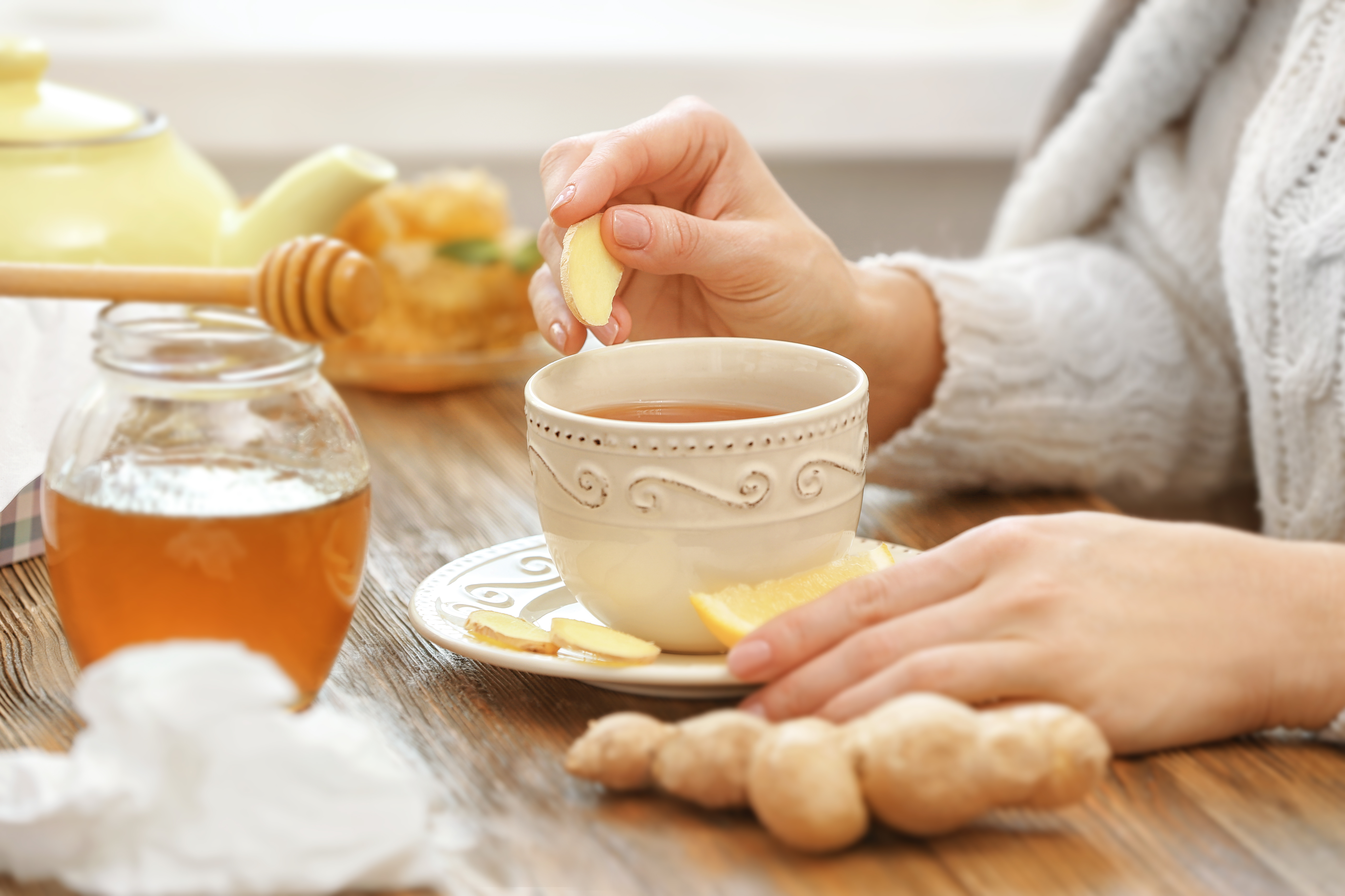 Woman with herbal cup of tea, surrounded by ginger, lemon, and honey.