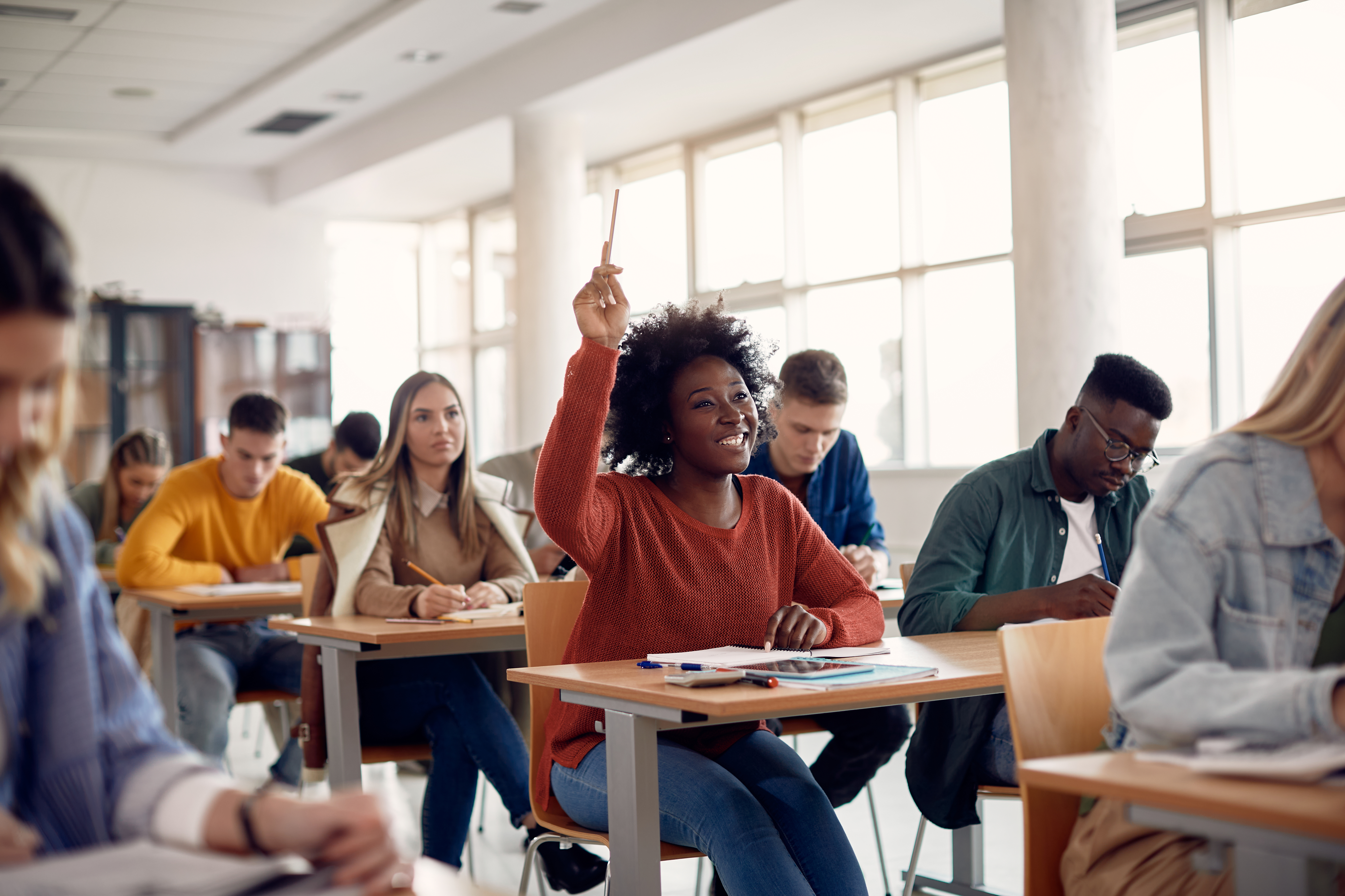 African American student raising her hand to ask a question during lecture in the classroom. 