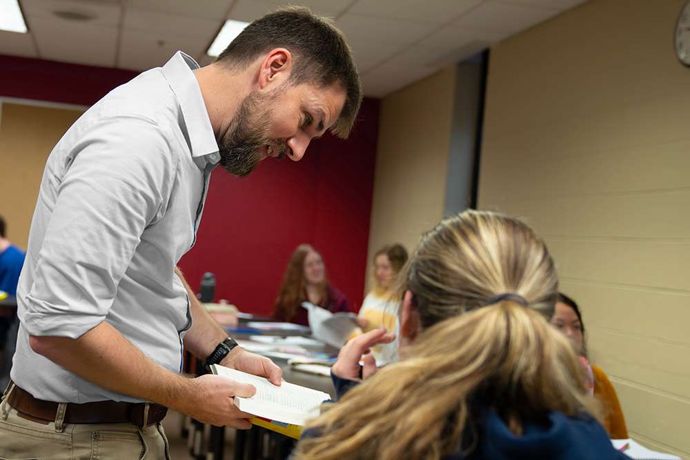 Two IWU educators smile beside a laptop in a classroom, representing Christ-centered mentorship and spiritual formation in education.