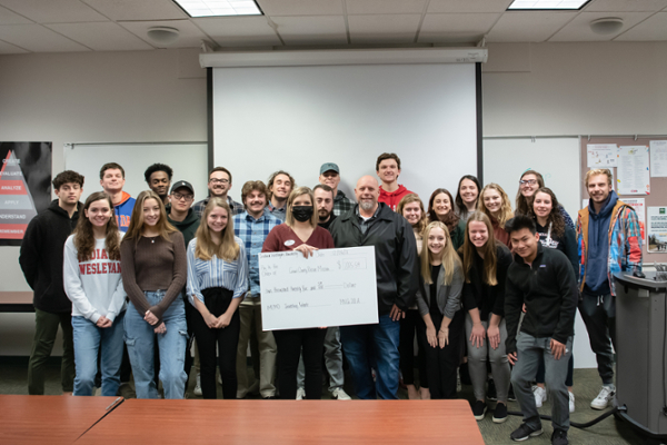 Business students stand in a classroom presenting a check for the Grant County Rescue Mission
