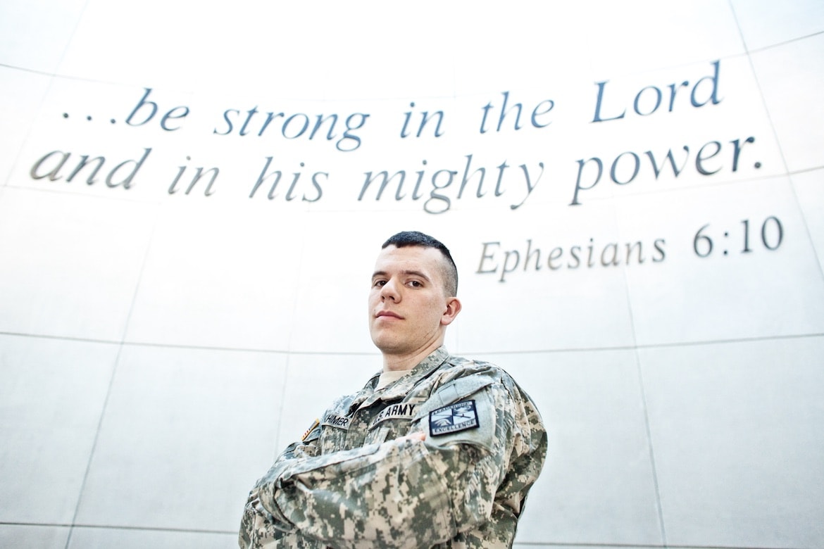 ROTC member in uniform stands with Bible verse in background