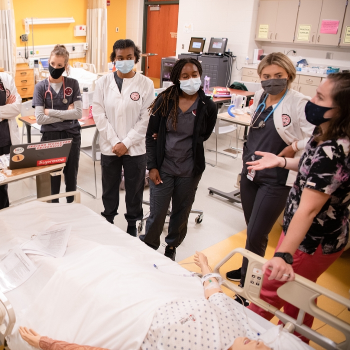 Nursing students gather around a training dummy in a hospital bed during class