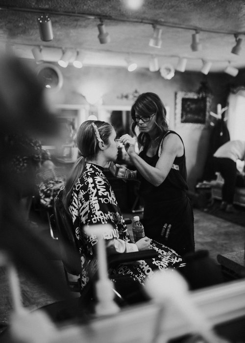 Photograph of a woman applying makeup to a woman sitting in a chair