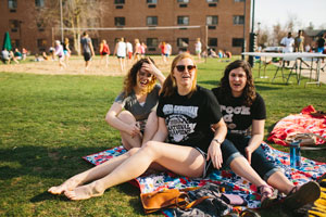 Three students sit with blanket on lawn for Spotted Cow event