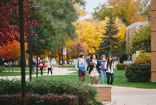 Four students walking on the IWU campus in the fall with colorful trees in the background